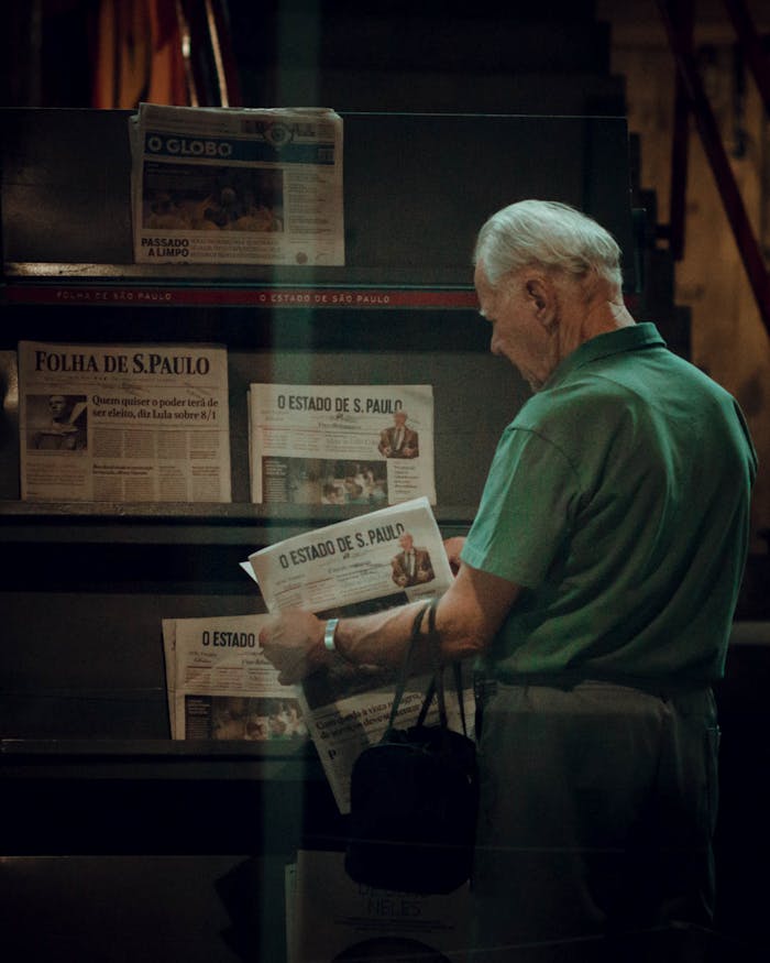 Senior adult browsing newspapers at a stand in São Paulo, Brazil. Captures urban life.